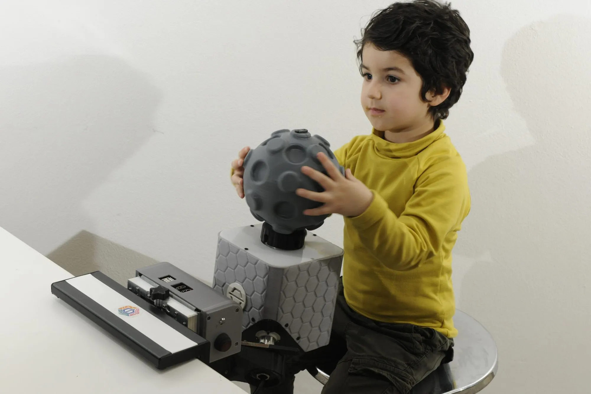 A boy holds the spherical Globo grip resting on top of a PhiCube unit clamped to a table.