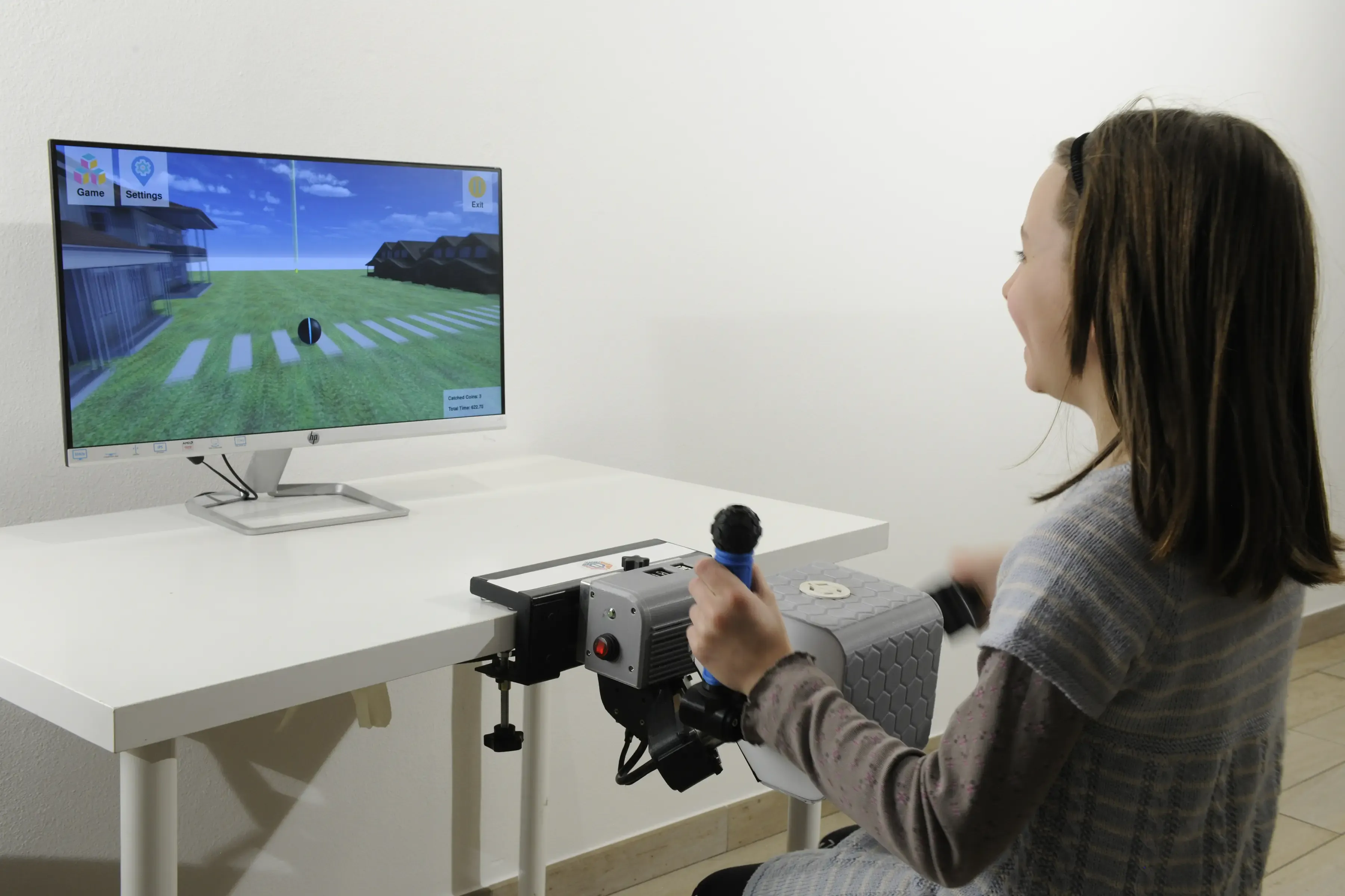 A girl laughs as she plays a PhiCube game, one hand on the grip of the unit on the table, the game on the screen in front of her.